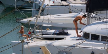 İtalya, Sicilya, Akdeniz, Marina di Ragusa (Ragusa ili); 22 Ağustos 2025, oğlu ile birlikte limandaki katamaran yelkenli teknesinde bir kadın - EDITORIAL