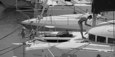 İtalya, Sicilya, Akdeniz, Marina di Ragusa (Ragusa ili); 22 Ağustos 2025, oğlu ile birlikte limandaki katamaran yelkenli teknesinde bir kadın - EDITORIAL