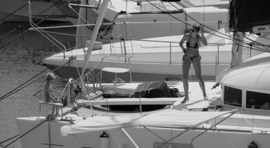 İtalya, Sicilya, Akdeniz, Marina di Ragusa (Ragusa ili); 22 Ağustos 2025, oğlu ile birlikte limandaki katamaran yelkenli teknesinde bir kadın - EDITORIAL