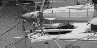 İtalya, Sicilya, Akdeniz, Marina di Ragusa (Ragusa ili); 22 Ağustos 2025, oğlu ile birlikte limandaki katamaran yelkenli teknesinde bir kadın - EDITORIAL