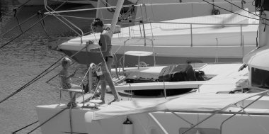 İtalya, Sicilya, Akdeniz, Marina di Ragusa (Ragusa ili); 22 Ağustos 2025, oğlu ile birlikte limandaki katamaran yelkenli teknesinde bir kadın - EDITORIAL