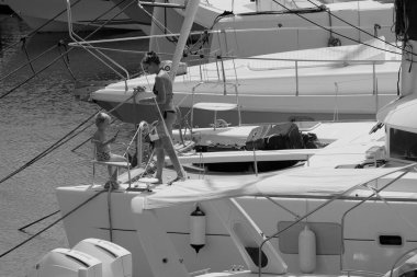 İtalya, Sicilya, Akdeniz, Marina di Ragusa (Ragusa ili); 22 Ağustos 2025, oğlu ile birlikte limandaki katamaran yelkenli teknesinde bir kadın - EDITORIAL