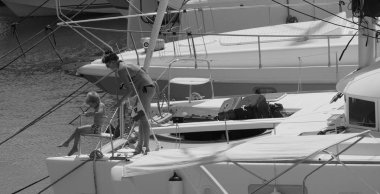 İtalya, Sicilya, Akdeniz, Marina di Ragusa (Ragusa ili); 22 Ağustos 2025, oğlu ile birlikte limandaki katamaran yelkenli teknesinde bir kadın - EDITORIAL