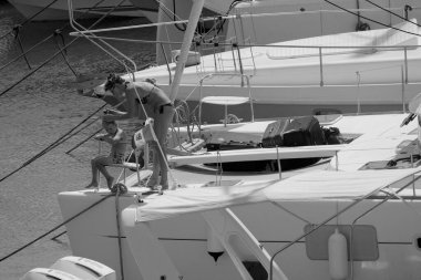 İtalya, Sicilya, Akdeniz, Marina di Ragusa (Ragusa ili); 22 Ağustos 2025, oğlu ile birlikte limandaki katamaran yelkenli teknesinde bir kadın - EDITORIAL