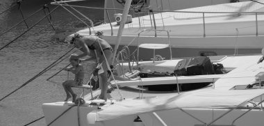 İtalya, Sicilya, Akdeniz, Marina di Ragusa (Ragusa ili); 22 Ağustos 2025, oğlu ile birlikte limandaki katamaran yelkenli teknesinde bir kadın - EDITORIAL