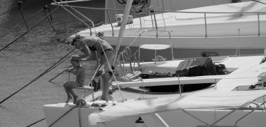 İtalya, Sicilya, Akdeniz, Marina di Ragusa (Ragusa ili); 22 Ağustos 2025, oğlu ile birlikte limandaki katamaran yelkenli teknesinde bir kadın - EDITORIAL