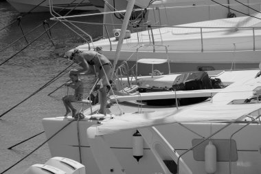 İtalya, Sicilya, Akdeniz, Marina di Ragusa (Ragusa ili); 22 Ağustos 2025, oğlu ile birlikte limandaki katamaran yelkenli teknesinde bir kadın - EDITORIAL