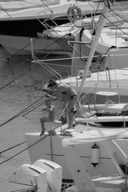 İtalya, Sicilya, Akdeniz, Marina di Ragusa (Ragusa ili); 22 Ağustos 2025, oğlu ile birlikte limandaki katamaran yelkenli teknesinde bir kadın - EDITORIAL