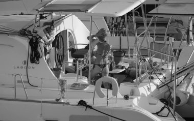 İtalya, Sicilya, Akdeniz, Marina di Ragusa (Ragusa ili); 24 Ağustos 2025, oğlu ile birlikte limanda katamaran yelkenli teknesinde bir kadın - EDITORIAL