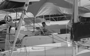 İtalya, Sicilya, Akdeniz, Marina di Ragusa (Ragusa Eyaleti); 25 Ağustos 2025, limandaki katamaran yelkenli teknesinde dizüstü bilgisayarı olan adam - EDITORIAL