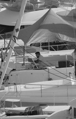 İtalya, Sicilya, Akdeniz, Marina di Ragusa (Ragusa Eyaleti); 25 Ağustos 2025, limandaki katamaran yelkenli teknesinde dizüstü bilgisayarı olan adam - EDITORIAL