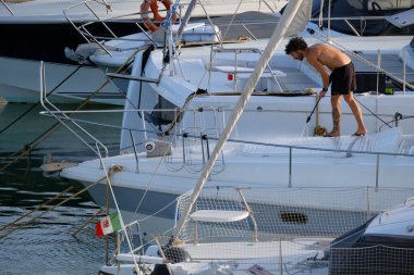 İtalya, Sicilya, Akdeniz, Marina di Ragusa (Ragusa ili); 30 Ağustos 2025; limanda lüks bir yatı temizleyen adam - EDITORIAL