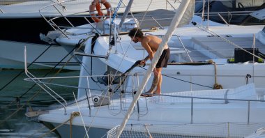 İtalya, Sicilya, Akdeniz, Marina di Ragusa (Ragusa ili); 30 Ağustos 2025; limanda lüks bir yatı temizleyen adam - EDITORIAL