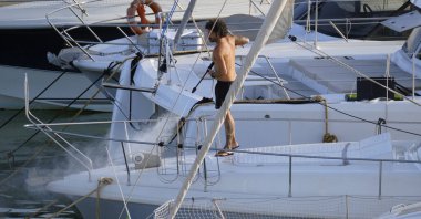 İtalya, Sicilya, Akdeniz, Marina di Ragusa (Ragusa ili); 30 Ağustos 2025; limanda lüks bir yatı temizleyen adam - EDITORIAL