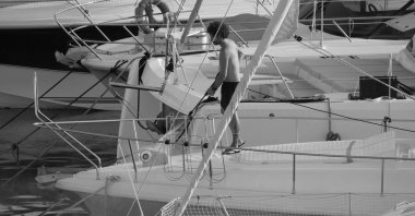 İtalya, Sicilya, Akdeniz, Marina di Ragusa (Ragusa ili); 30 Ağustos 2025; limanda lüks bir yatı temizleyen adam - EDITORIAL