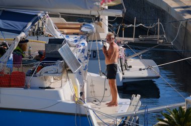 İtalya, Sicilya, Akdeniz, Marina di Ragusa (Ragusa Eyaleti); 31 Ağustos 2025, limanda katamaran yelkenli teknesini temizleyen adam - EDITORIAL