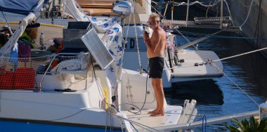 İtalya, Sicilya, Akdeniz, Marina di Ragusa (Ragusa Eyaleti); 31 Ağustos 2025, limanda katamaran yelkenli teknesini temizleyen adam - EDITORIAL