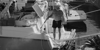 İtalya, Sicilya, Akdeniz, Marina di Ragusa (Ragusa Eyaleti); 31 Ağustos 2025, limanda katamaran yelkenli teknesini temizleyen adam - EDITORIAL