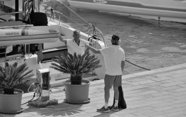 İtalya, Sicilya, Akdeniz, Marina di Ragusa (Ragusa Eyaleti); 1 Ekim 2025, limanda insanlar ve bir katamaran yelkenli teknesi - EDITORIAL