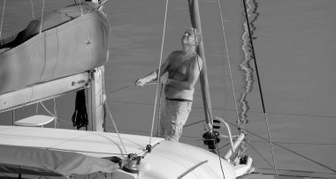 İtalya, Sicilya, Akdeniz, Marina di Ragusa (Ragusa Eyaleti); 1 Ekim 2025, limandaki bir katamaran yelkenli teknesinde adam - EDITORIAL