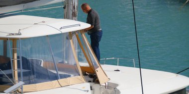 İtalya, Sicilya, Akdeniz, Marina di Ragusa (Ragusa Eyaleti); 3 Ekim 2025, limandaki bir katamaran yelkenli teknesindeki adam - EDITORIAL