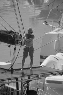 İtalya, Sicilya, Akdeniz, Marina di Ragusa (Ragusa Eyaleti); 5 Ekim 2025, limandaki bir katamaran yelkenli teknesinde adam - EDITORIAL