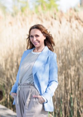 Güneşli bir bahar öğleden sonrasında orta yaşlı güzel bir kadın doğada poz veriyor. Güneş ışığı ve ağaçların gölgelerinin etkileşimi görsel bir etki yaratır..