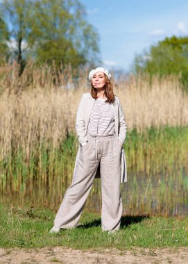 Güneşli bir bahar öğleden sonrasında orta yaşlı güzel bir kadın doğada poz veriyor. Güneş ışığı ve ağaçların gölgelerinin etkileşimi görsel bir etki yaratır..