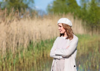 Güneşli bir bahar öğleden sonrasında orta yaşlı güzel bir kadın doğada poz veriyor. Güneş ışığı ve ağaçların gölgelerinin etkileşimi görsel bir etki yaratır..
