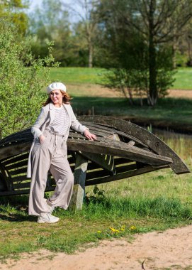 Güneşli bir bahar öğleden sonrasında orta yaşlı güzel bir kadın doğada poz veriyor. Güneş ışığı ve ağaçların gölgelerinin etkileşimi görsel bir etki yaratır..