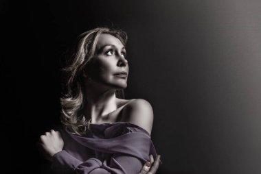 Gri arka planda duran zarif olgun yaşlı kadın. Kendinden emin, orta yaşlı, neşeli, 50 'li yaşlarda bir kadın..