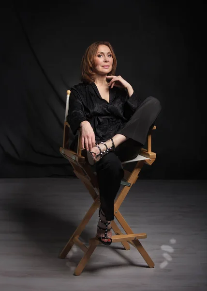 Schöne Frau Sitzt Auf Einem Stilvollen Hölzernen Regiestuhl Auf Schwarzem — Stockfoto