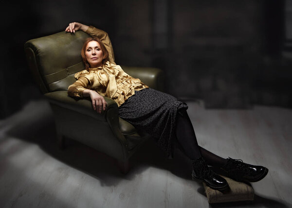 Взрослая элегантная женщина в кресле. Портрет взрослой женщины в элегантном наряде, расслабляющей дома.