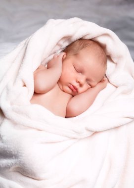 Yeni doğan bebek rahat etmek için küçük parmaklarını başparmağına dolamış yumuşak beyaz bir battaniyenin üzerinde huzur içinde uyuyor. Sakin yüzleri ve nazik göğüs hareketleri onları değerli gösteriyor.