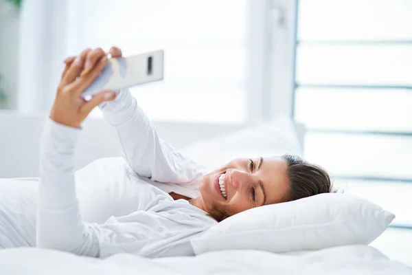 床上挂着智能手机的年轻黑发女人高质量的照片 — 图库照片