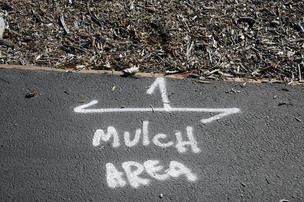 Mulch Area. Spray Paint Words on the blacktop that read MULCH AREA. White Spray Painted Words. Garden Mulch. Black Top Cement. Sidewalk. Walkway