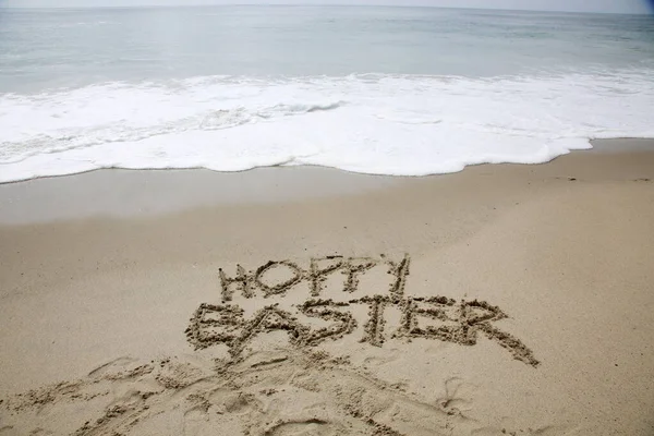 ビーチの砂の中に書かれた幸せなイースター 滑らかな砂浜に手書きのメッセージ — ストック写真