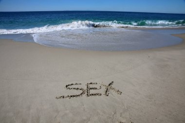 sex written in the sand on the beach.  message handwritten on a smooth sand beach