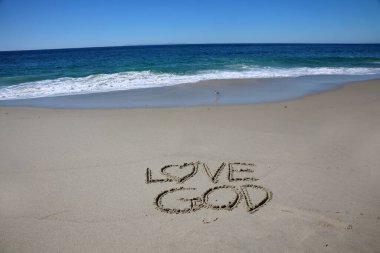 love god written in the sand on the beach.  message handwritten on a smooth sand beach 