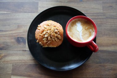 Latte with a Banana Walnut Muffin. Coffee with a Muffin on a black plate in a Coffee Shop. Breakfast Muffin and Coffee with Latte Art in the foam for breakfast or a snack in a Coffee Shop. Breakfast.
