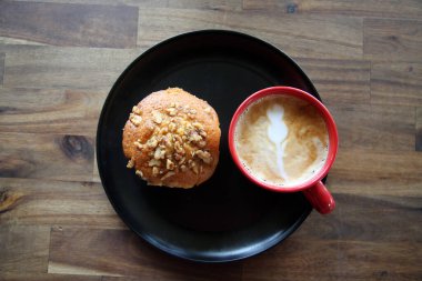 Latte with a Banana Walnut Muffin. Coffee with a Muffin on a black plate in a Coffee Shop. Breakfast Muffin and Coffee with Latte Art in the foam for breakfast or a snack in a Coffee Shop. Breakfast.