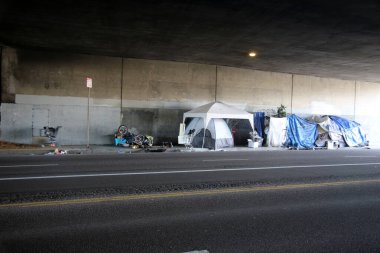 Long Beach, California - ABD - 16 Nisan 2023: Trafik şeridinde bir duvara karşı evsiz barınağı. Evsizlik toplum ve yoksulluktan etkilenen insanlar için ulusal bir sorun haline geldi..