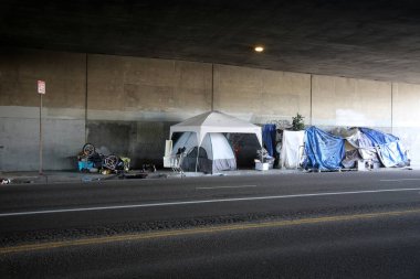 Long Beach, California - ABD - 16 Nisan 2023: Trafik şeridinde bir duvara karşı evsiz barınağı. Evsizlik toplum ve yoksulluktan etkilenen insanlar için ulusal bir sorun haline geldi..