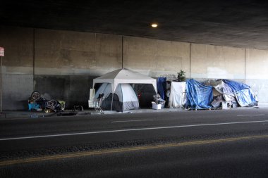 Long Beach, California - ABD - 16 Nisan 2023: Trafik şeridinde bir duvara karşı evsiz barınağı. Evsizlik toplum ve yoksulluktan etkilenen insanlar için ulusal bir sorun haline geldi..