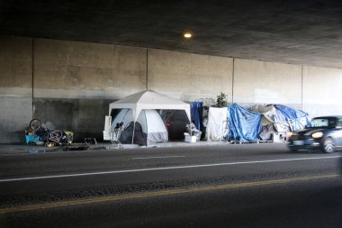Long Beach, California - ABD - 16 Nisan 2023: Trafik şeridinde bir duvara karşı evsiz barınağı. Evsizlik toplum ve yoksulluktan etkilenen insanlar için ulusal bir sorun haline geldi..