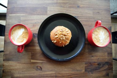 Latte with a Banana Walnut Muffin. Coffee with a Muffin on a black plate in a Coffee Shop. Breakfast Muffin and Coffee with Latte Art in the foam for breakfast or a snack in a Coffee Shop. Breakfast.