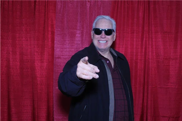 Photo Booth. A man smile and poses for his photo to be taken while in a Photo Booth with a Red Curtain background. People love Photo Booths and enjoy them at parties and other events all year long.