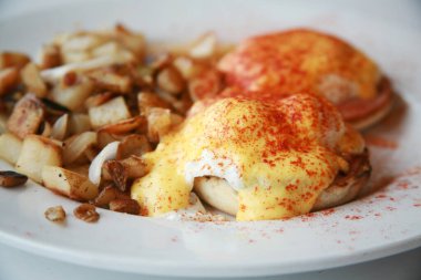 Benedict usulü yumurta. Kahvaltıda. Haşlanmış yumurta ve ızgara patates. Peynir soslu yumurta ve soğan ve biberli patates kahvaltısı. Kahvaltı mı yoksa Restoranda Kahvaltı mı? Sabah Kahvaltısı.