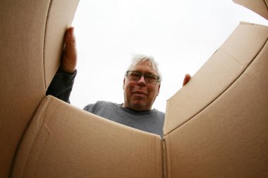 Karton kutuyu açıyorum. Gülümseyen adam bir karton kutuyu açıyor, yer değiştiriyor ve paketleri açıyor. Teslimat kavramı, sürpriz, hediye, karton kutuyu açan kişi. Şaşırmış bir adam bir kutuyu açıyor..