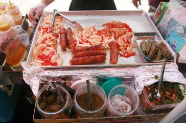 Food. Bacon Wrapped Hot Dogs. Grilled Onions and Peppers. Hot Dog Cart. Food Cart. Hot Dogs being cooked and offered for sale on the side walk of Hollywood California. Hungry Tourist enjoy Hot Dogs. clipart